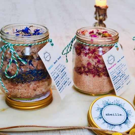 Two jars of bath salts with decorative elements and labels on a marble surface.