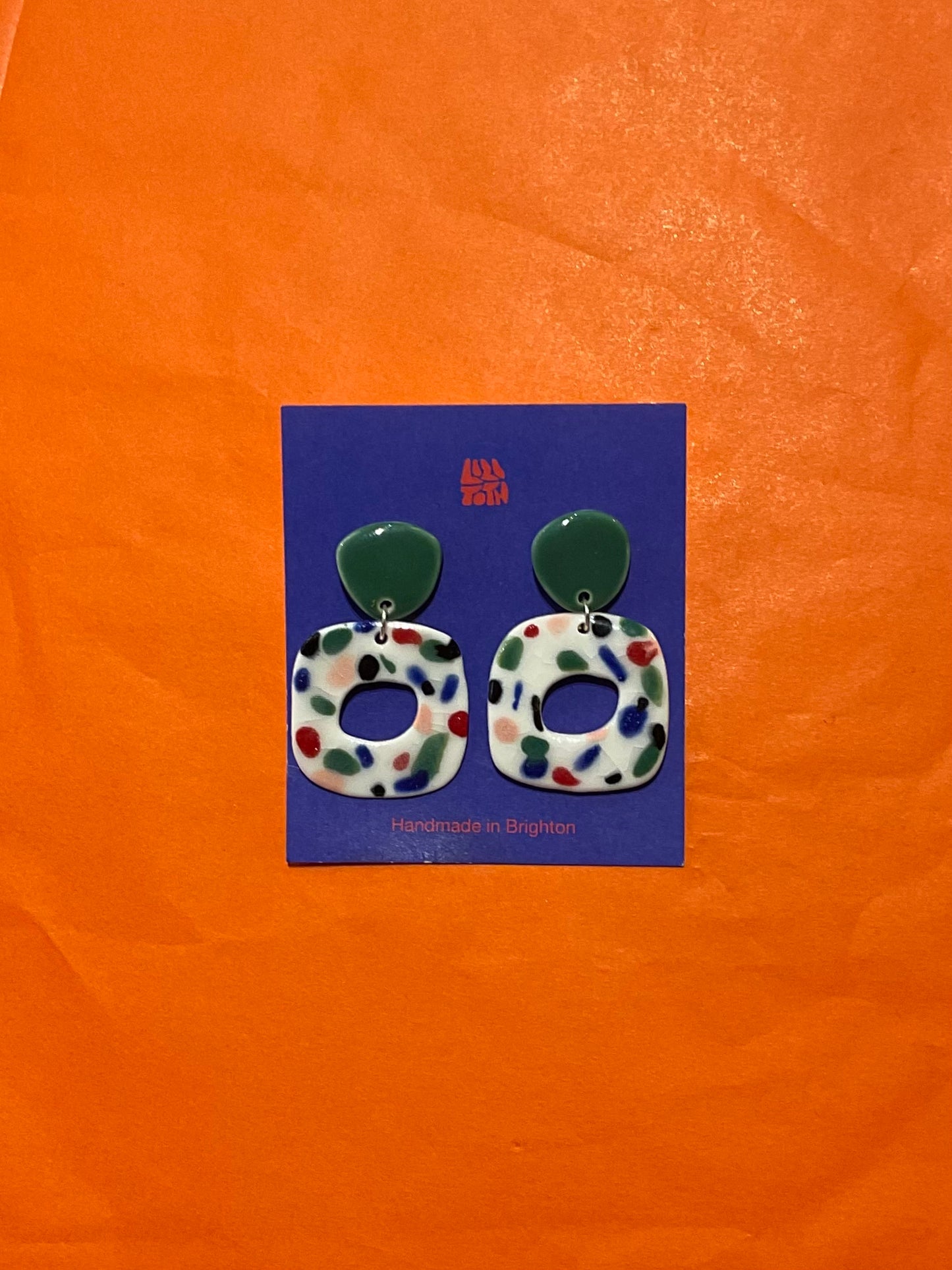 Pair of earrings on a blue card with an orange background