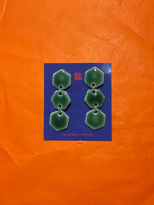 Green earrings on a blue card with 'Handmade in Brighton' text, against an orange background