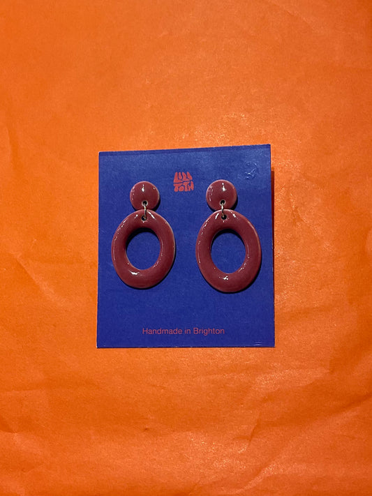 Pair of maroon hoop earrings on a blue card with 'Handmade in Brighton' text, against an orange background.