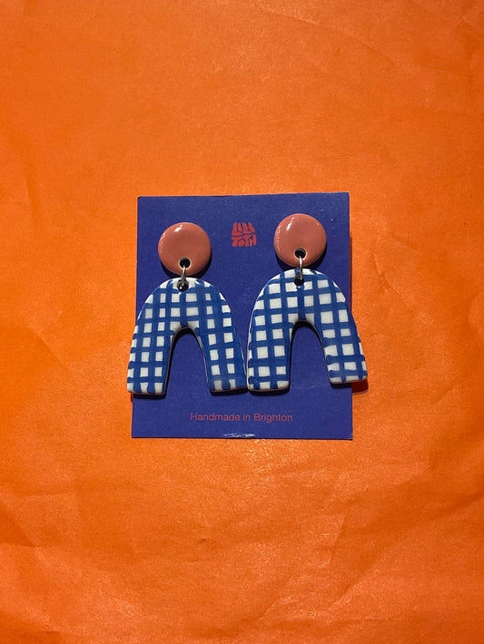 Earrings with blue and white checkered design on a blue card against an orange background