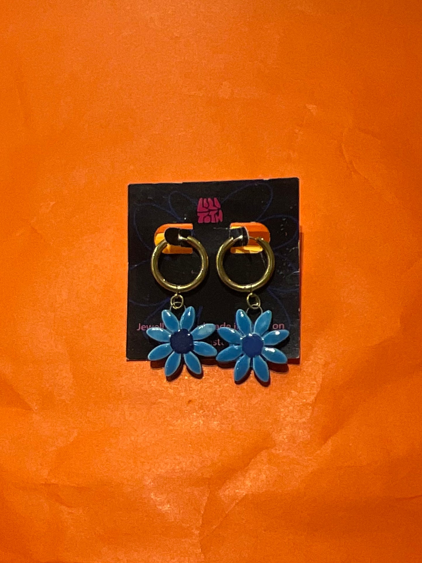 Blue flower-shaped earrings on a black card against an orange background