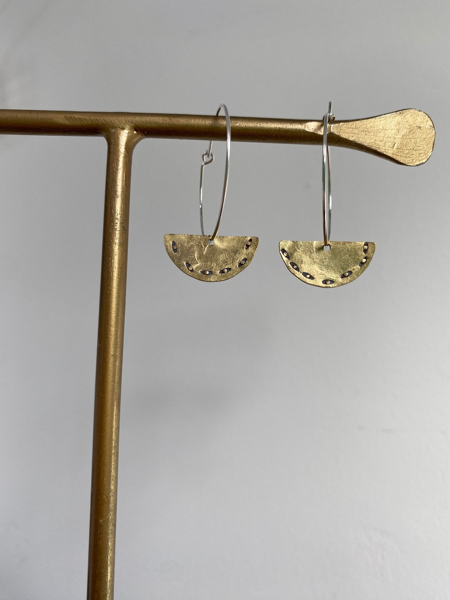 Gold hoop earrings with half-circle designs hanging on a gold stand against a gray background
