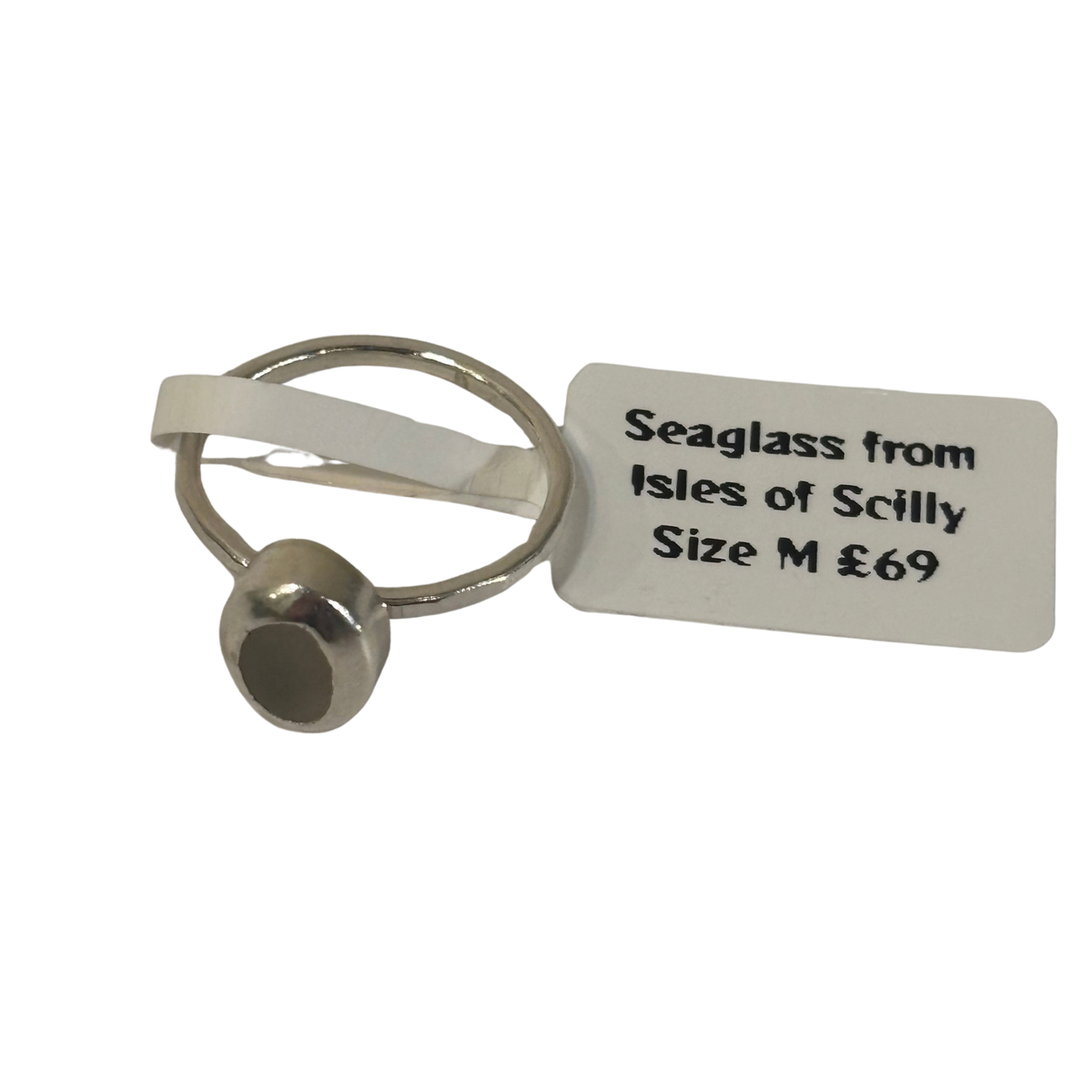 A small silver-toned seaglass ring with a white paper tag attached, reading 'Seaglass from Isles of Scilly Size M £69', on a plain white background.