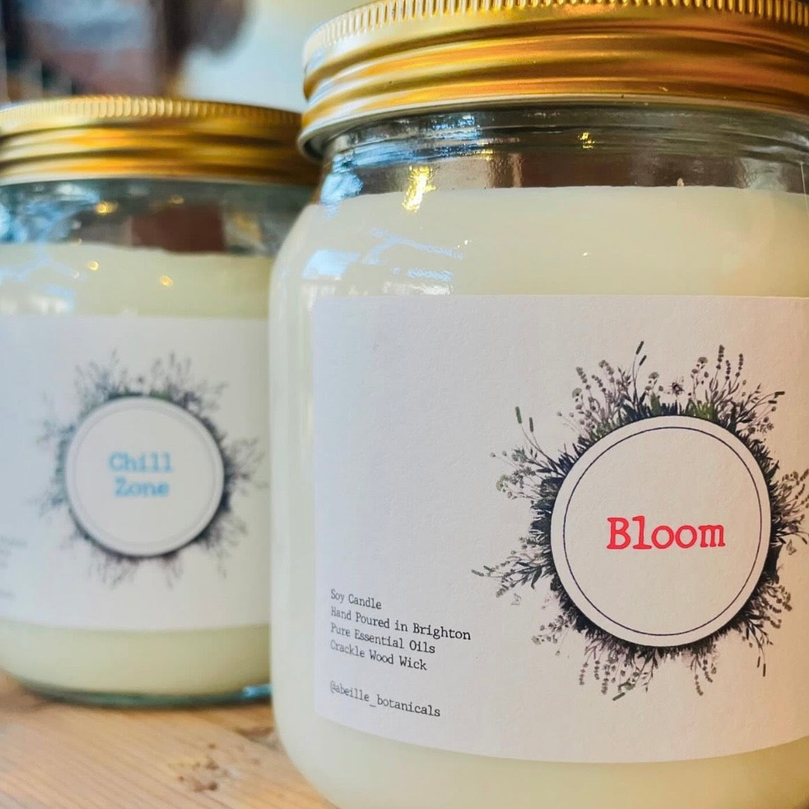 Two candles in glass jars with labels on a wooden surface