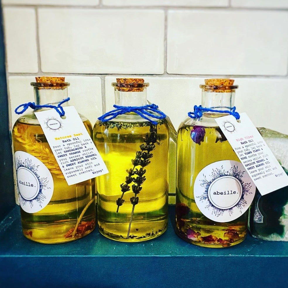 Three bottles of abeille essential oils with labels on a blue surface.