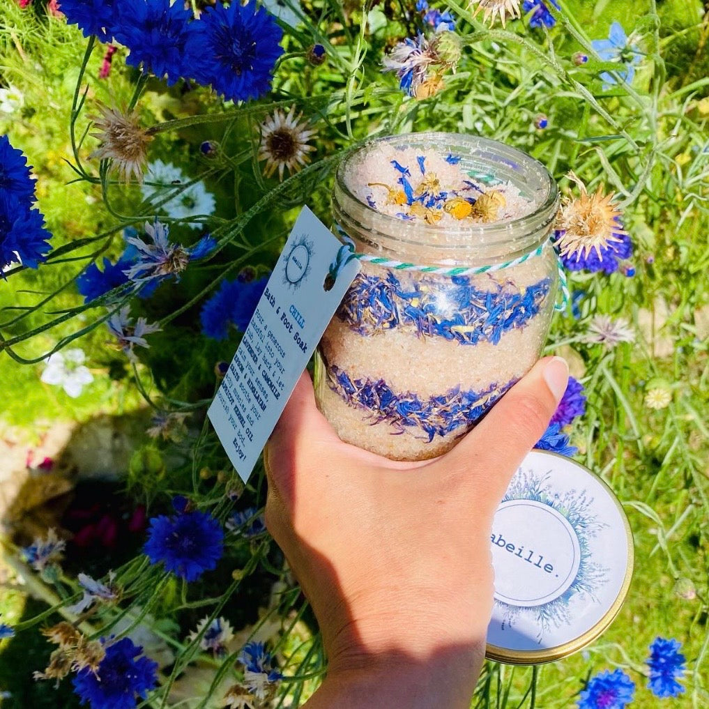 Hand holding a jar of bath salts with flowers in the background