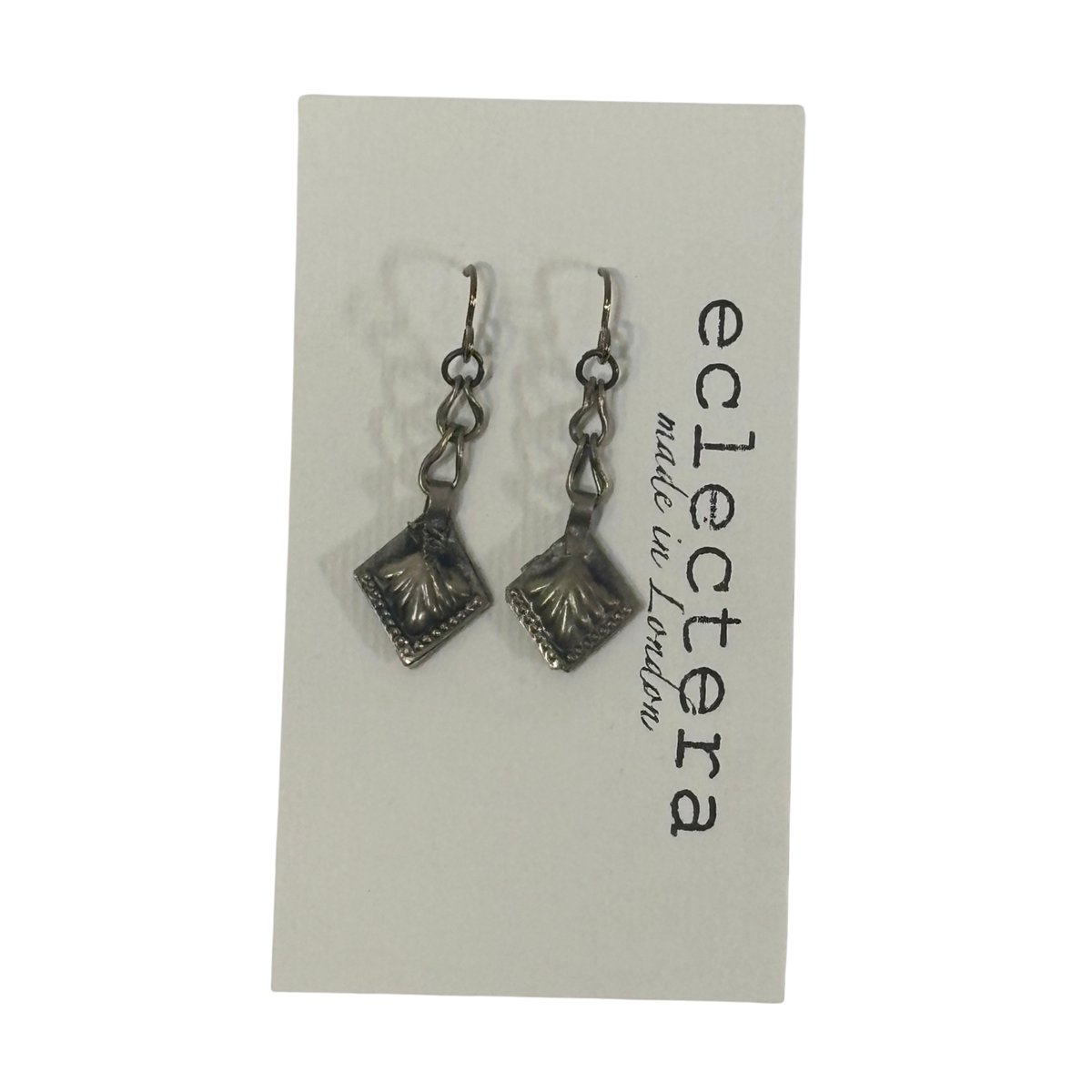 A pair of silver-toned dangle earrings with textured square charms, displayed on a white card printed with the brand name 'eclectera made in London'.