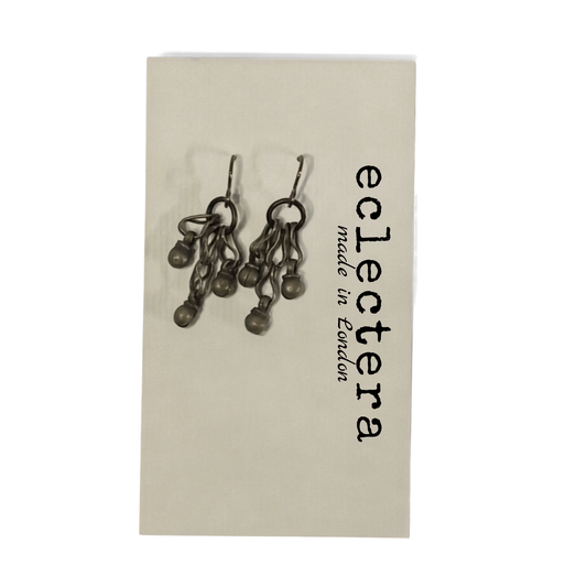 A pair of dark metallic dangle earrings displayed on a cream-colored backing card printed with the brand name 'eclectera' and 'made in London'.