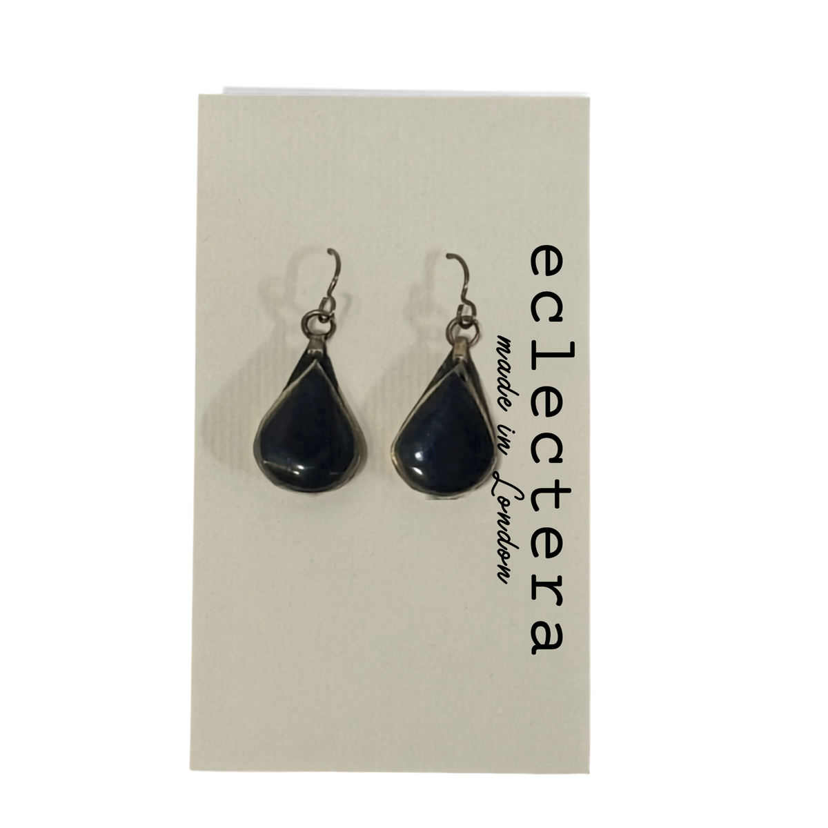 A pair of teardrop-shaped dark blue glass drop earrings with silver-toned hooks, displayed on a cream-colored card printed with the brand name 'eclectera'.