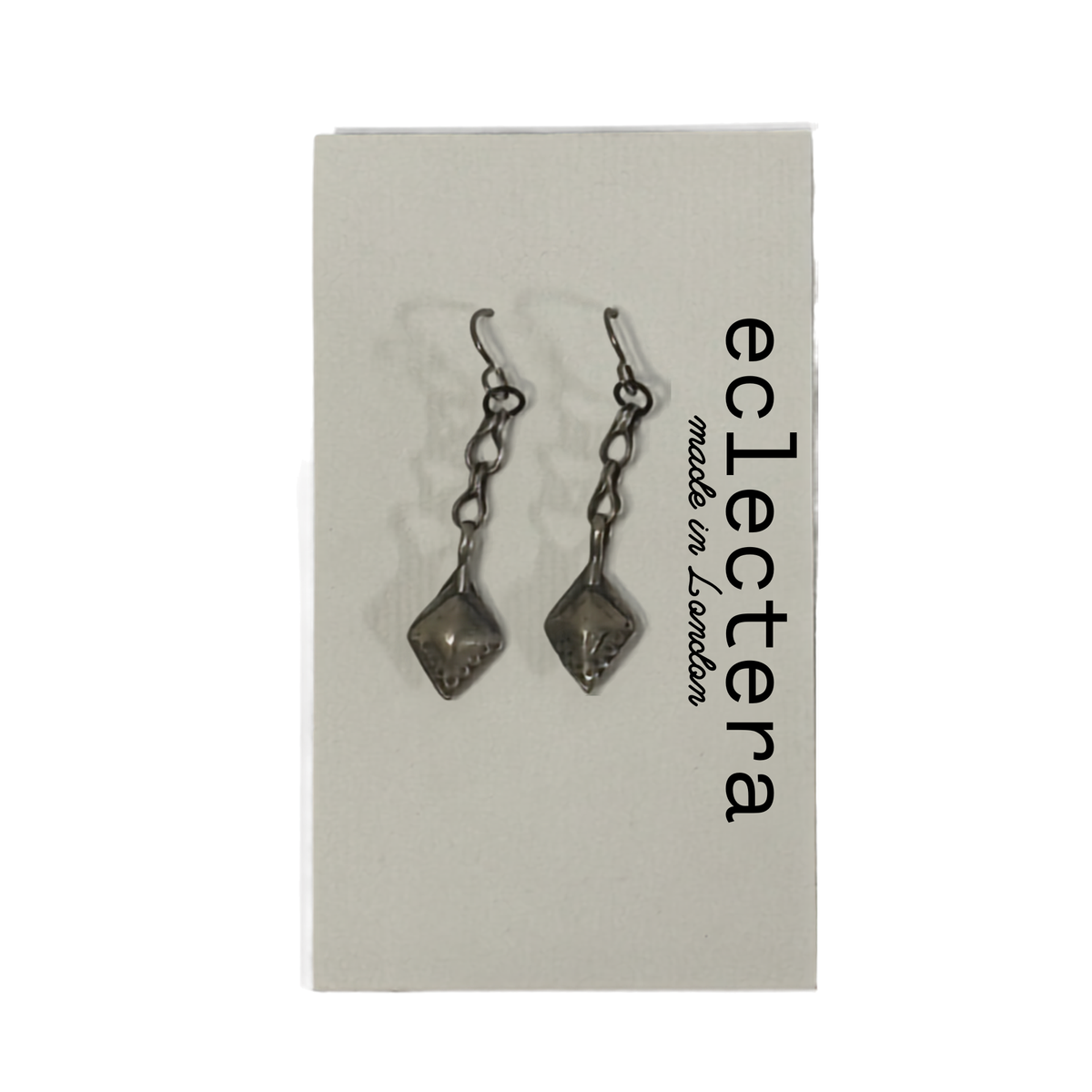A pair of dark metallic drop earrings with faceted diamond-shaped charms, displayed on a light gray brand card that reads 'eclectera made in London'.