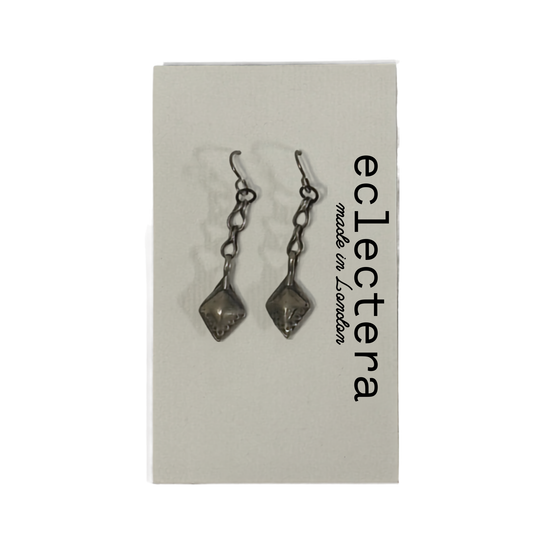 A pair of dark metallic drop earrings with faceted diamond-shaped charms, displayed on a light gray brand card that reads 'eclectera made in London'.
