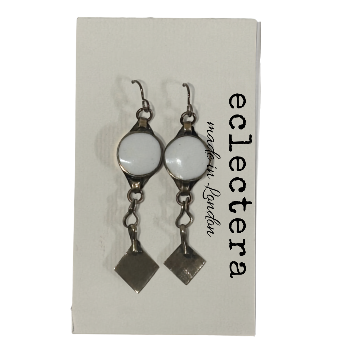 A pair of silver-toned dangle earrings with oval white stones and dangling square charms, displayed on a white card printed with the brand name 'eclectera'.
