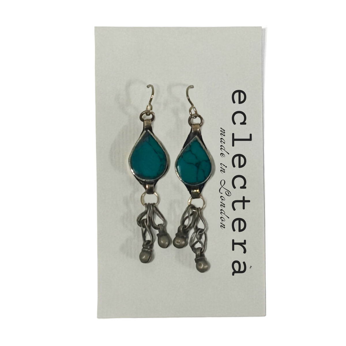 A pair of silver-toned dangle earrings with teardrop-shaped turquoise-blue stones, displayed on a white brand card that reads 'eclectera made in London'.