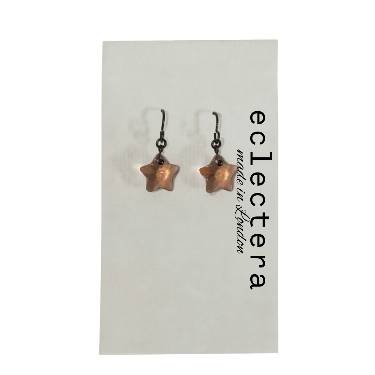 A pair of star-shaped drop earrings with dark metal hooks and a warm copper or rose-gold toned center, displayed on a white card printed with the brand name 'eclectera made in London'.