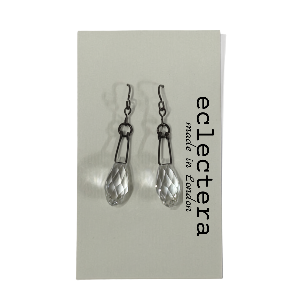 A pair of silver-toned drop earrings with faceted clear teardrop-shaped crystal pendants, displayed on a light gray card printed with the brand name 'eclectera made in London'.