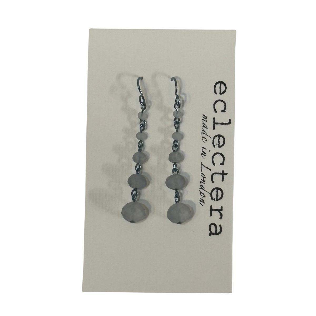 A pair of silver-toned dangle earrings with faceted gray beads, displayed on a beige backing card printed with the brand name 'eclectera made in London'.