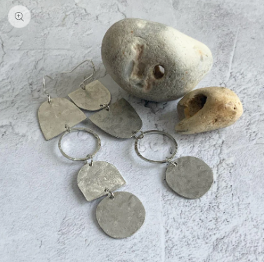 Silver drop earrings n a textured gray surface with stones.