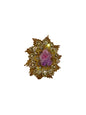 Decorative brooch with gold detailing and a pink and purple flower on a wooden surface.
