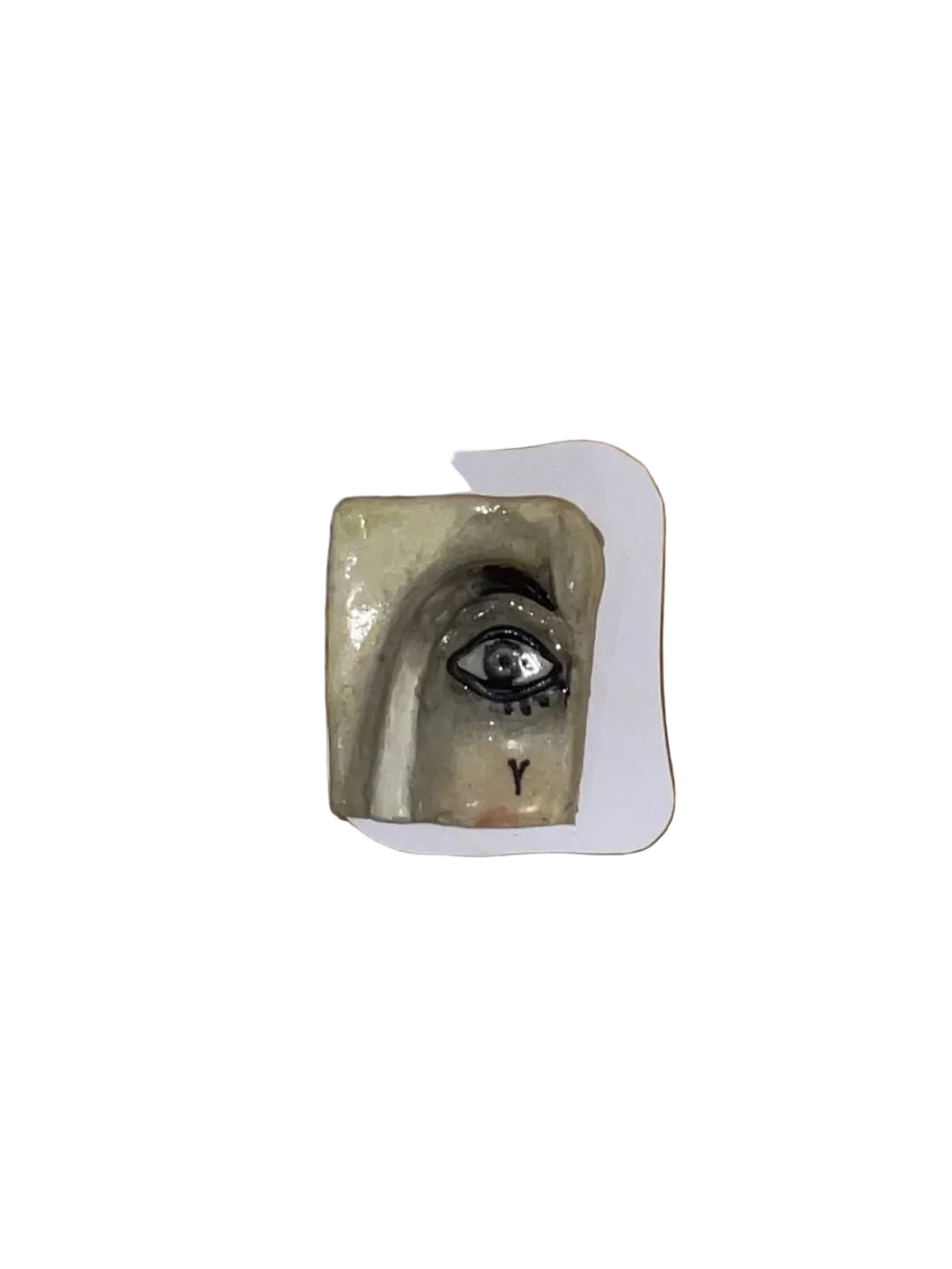 Small ceramic piece with a face design on a white card, against a wooden background