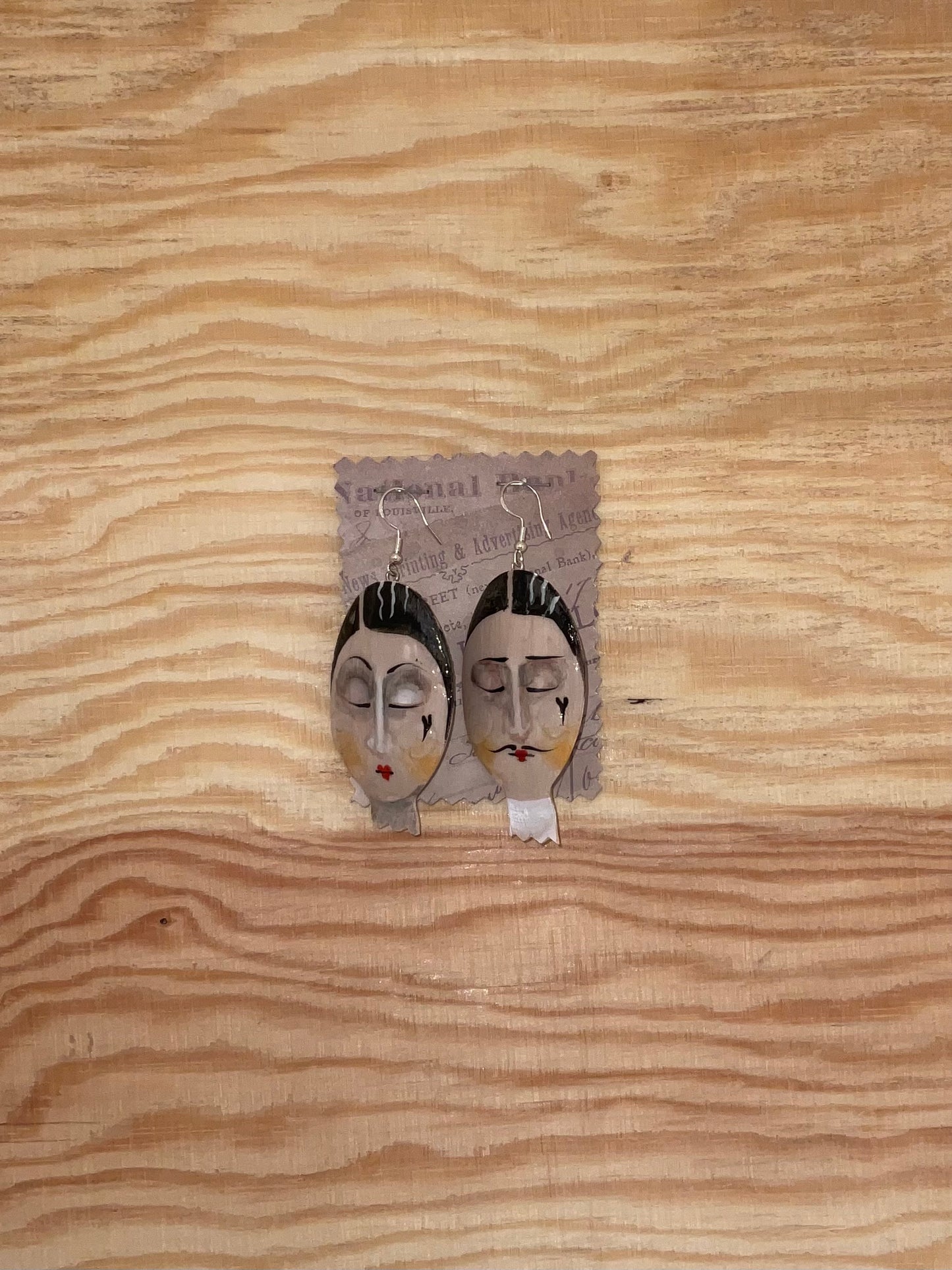 Pair of earrings with face designs on a wooden surface