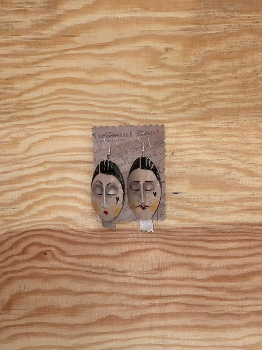 Pair of earrings with face designs on a wooden surface