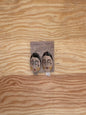 Pair of earrings with face designs on a wooden surface