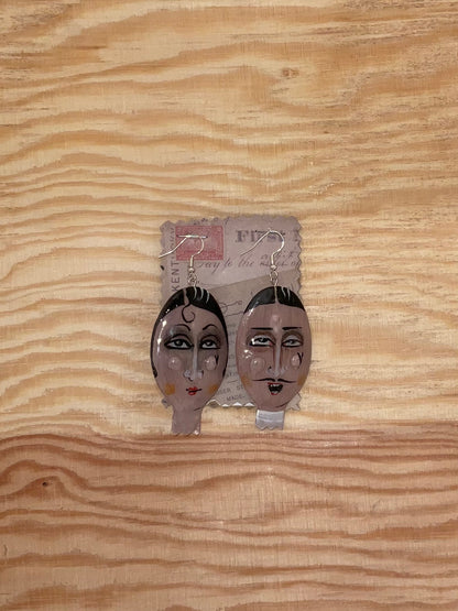Pair of earrings with face designs on a wooden surface
