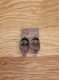 Pair of earrings with face designs on a wooden surface