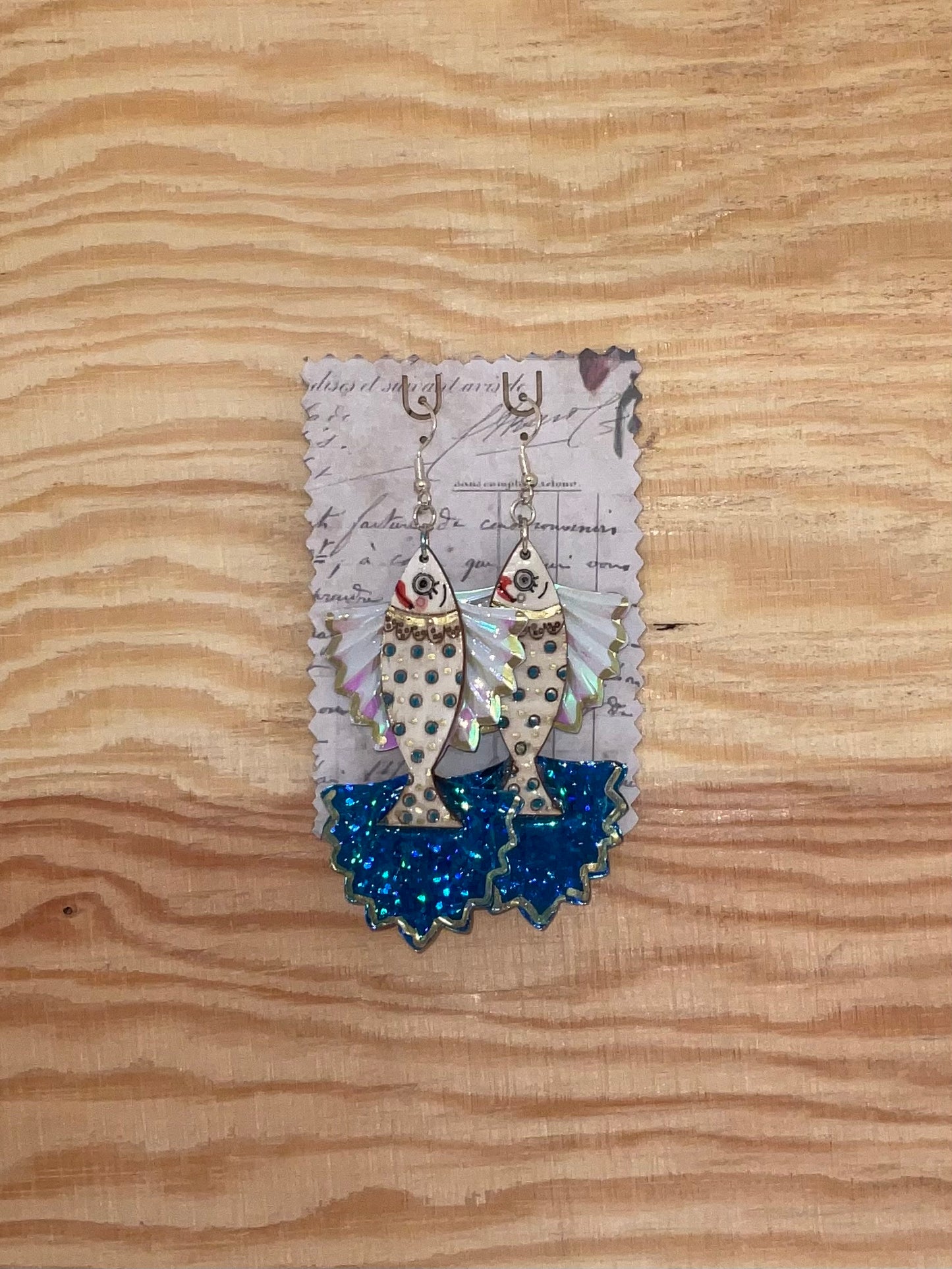 Fish-shaped earrings with blue accents on a wooden surface