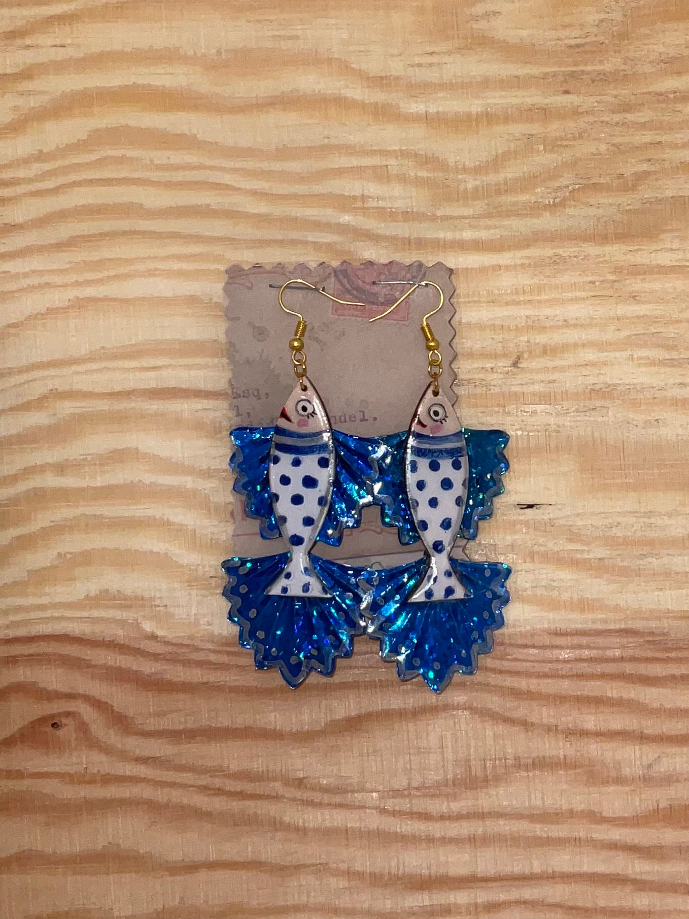 Blue and white fish-shaped earrings on a wooden surface