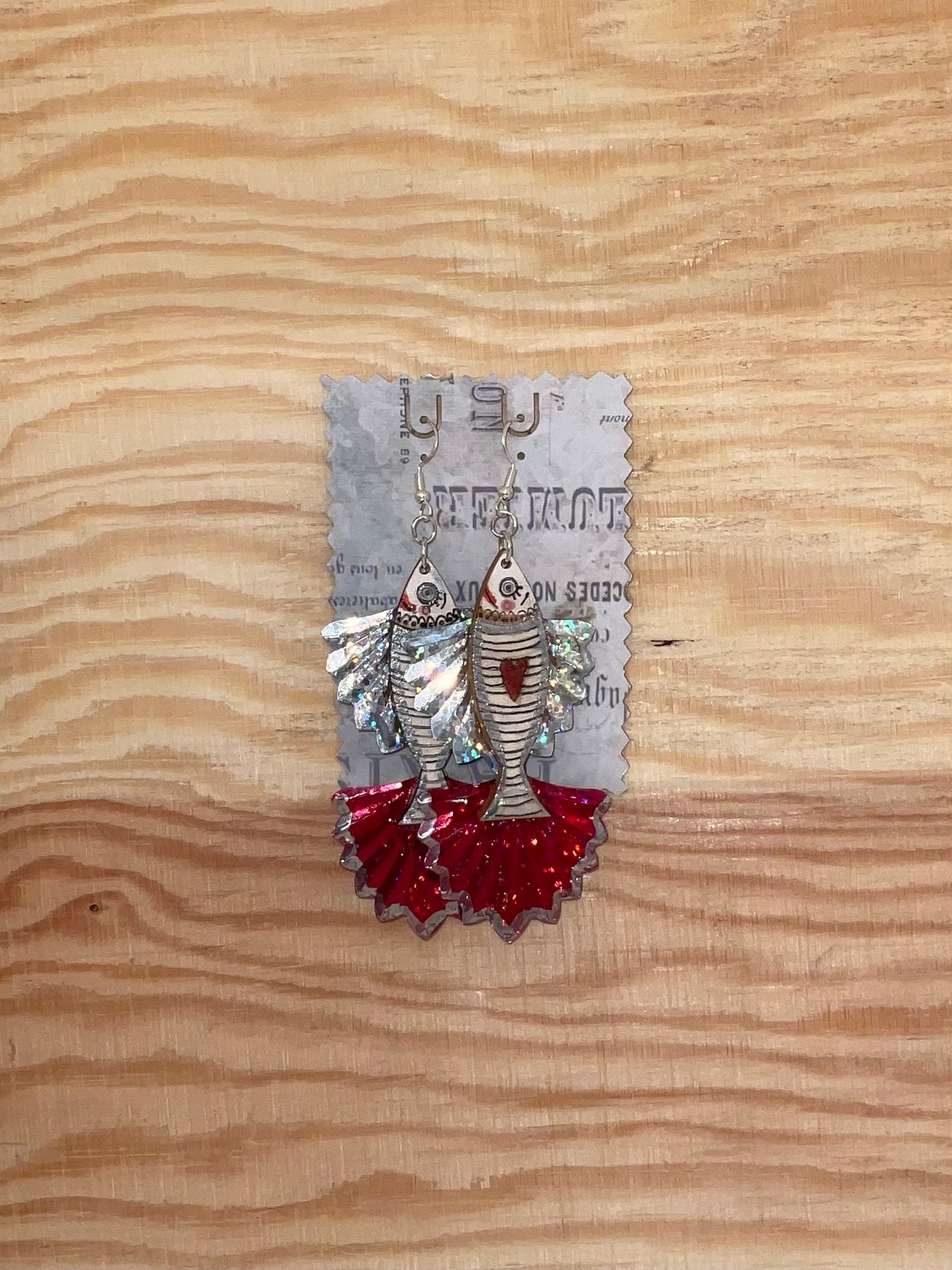 Pair of silver earrings with red accents on a decorative card against a wooden background