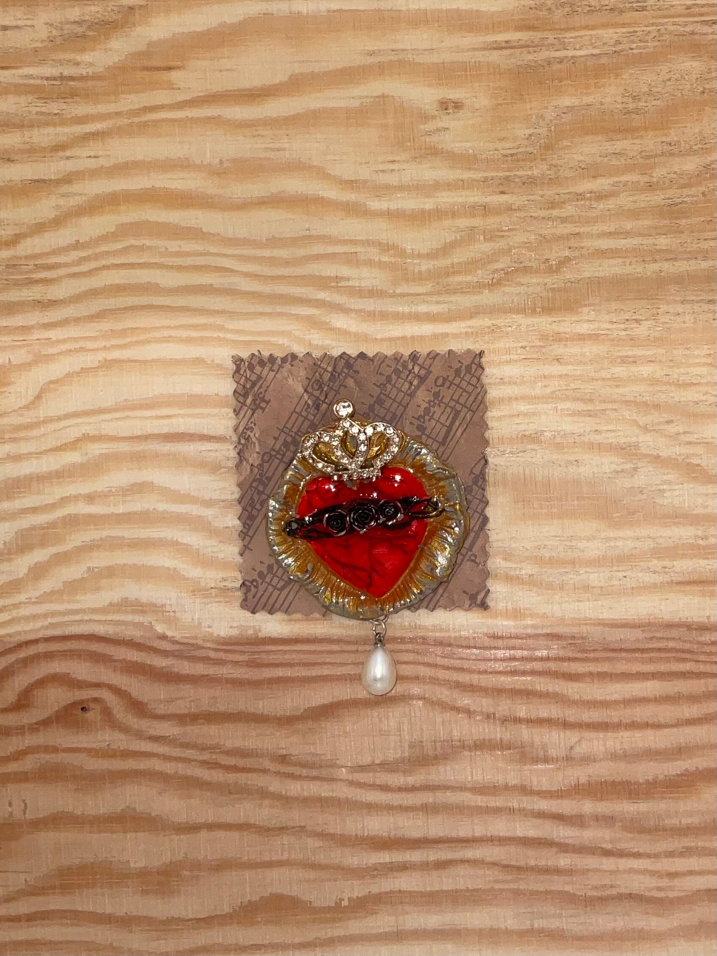 Heart-shaped brooch with red center and gold accents on a textured fabric background