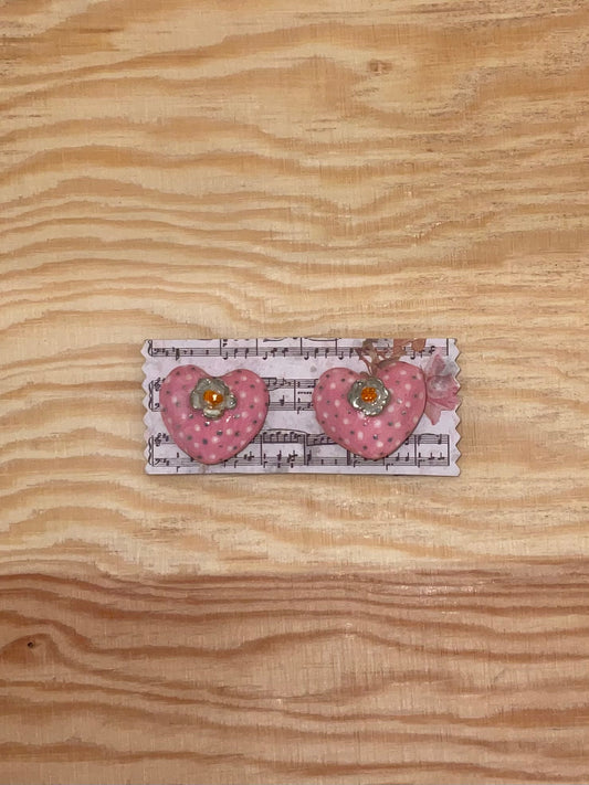 Heart-shaped hair clips on a card with music notes on a wooden surface