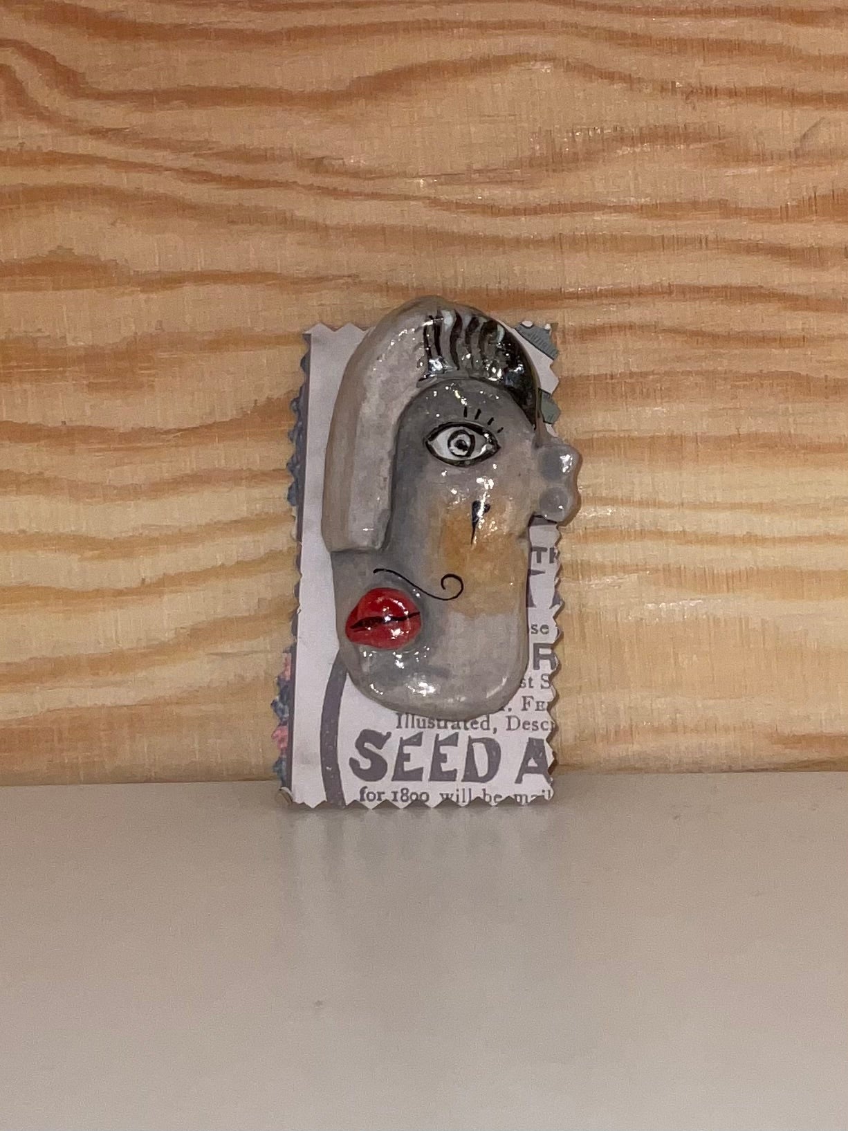 Metallic sculpture of a face on a seed packet against a wooden background