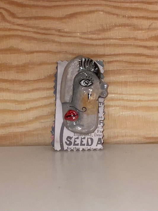 Metallic sculpture of a face on a seed packet against a wooden background