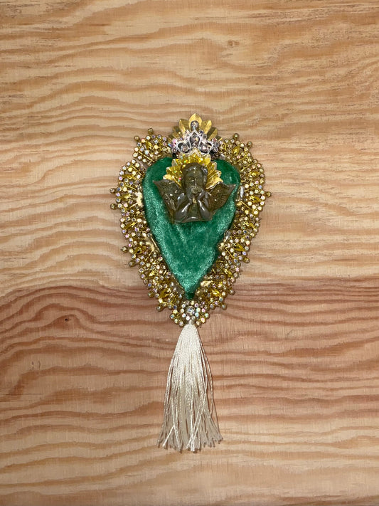 Decorative brooch with green heart and gold detailing on a wooden surface
