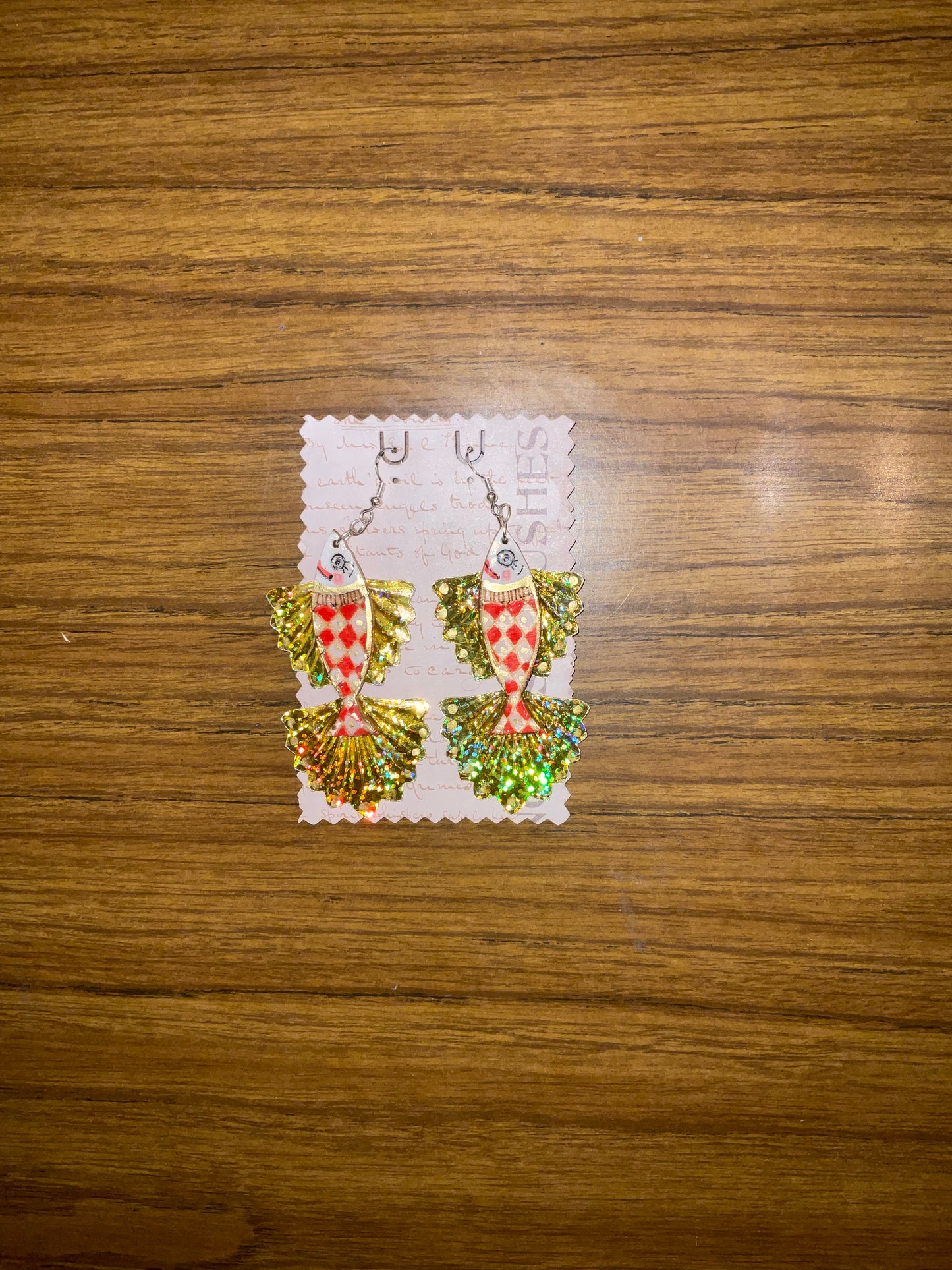 Pair of fish-shaped earrings on a decorative card against a wooden background
