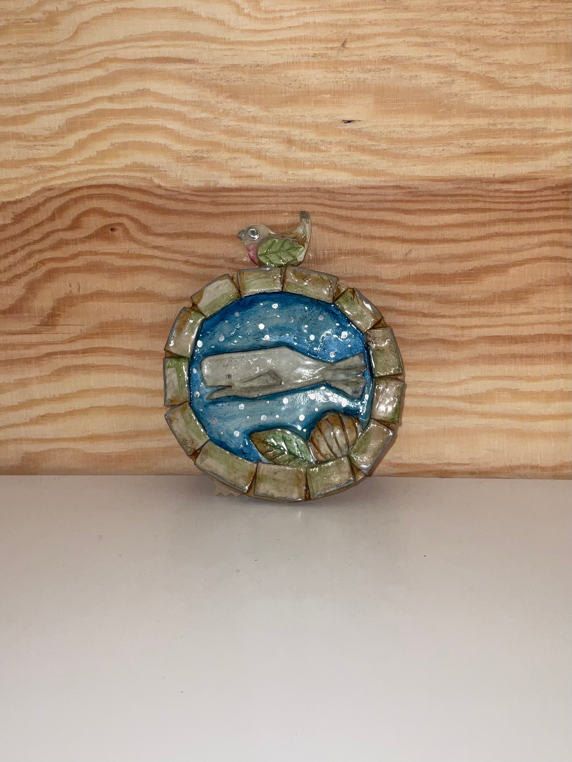 Decorative brooch with a bird and landscape design on a wooden surface