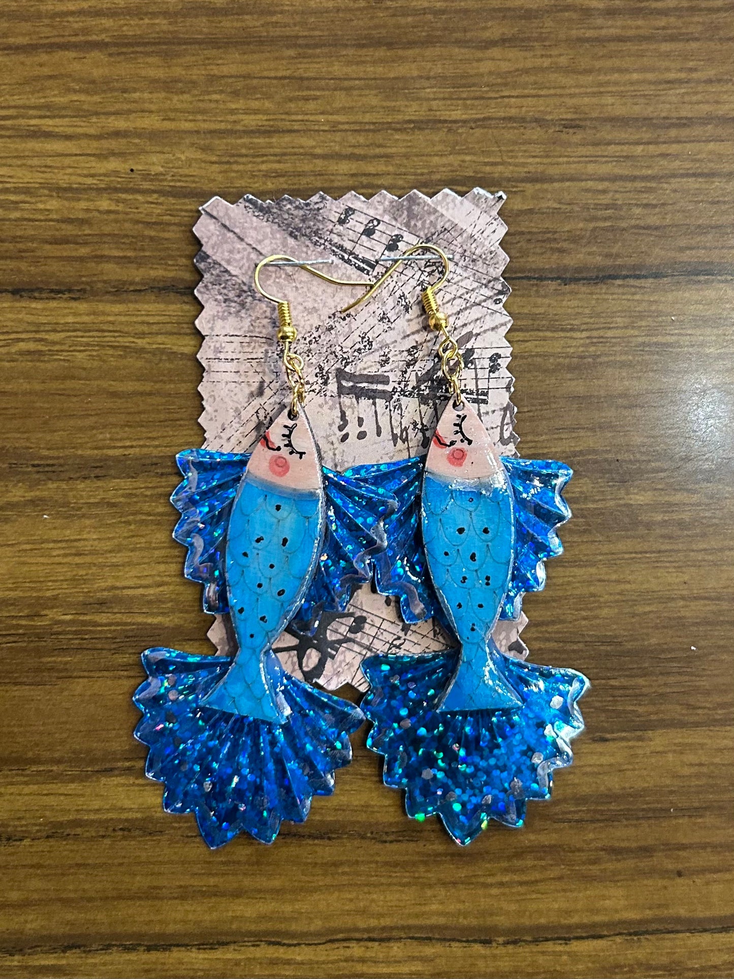 Blue fish-shaped earrings on a decorative card with music notes on a wooden surface