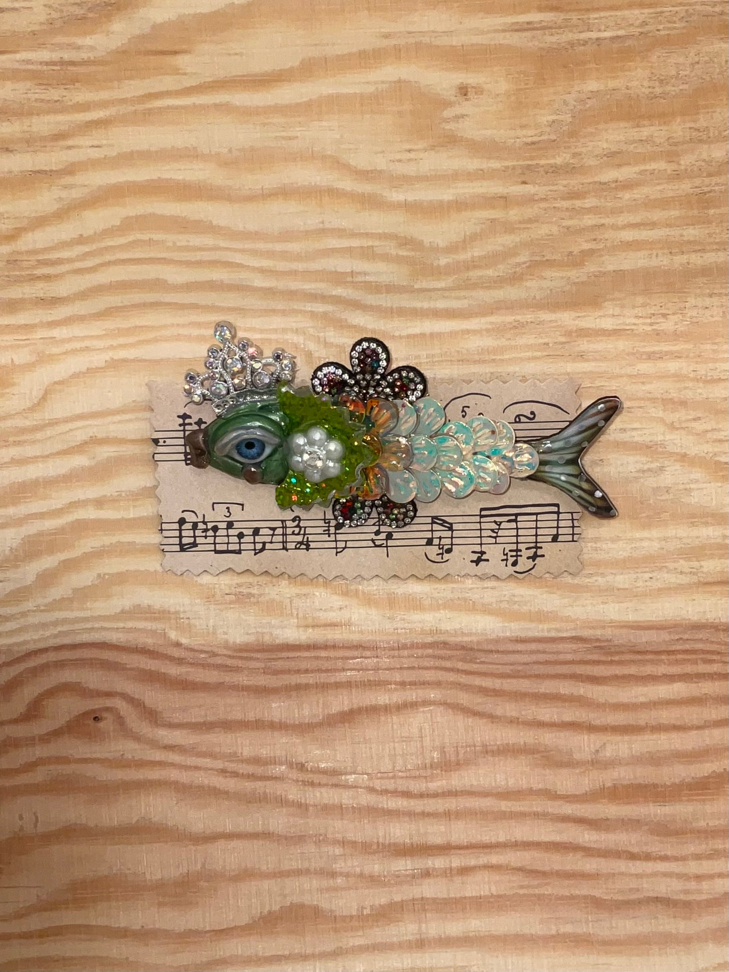 Decorative fish-shaped object with floral elements and musical notes on a wooden surface