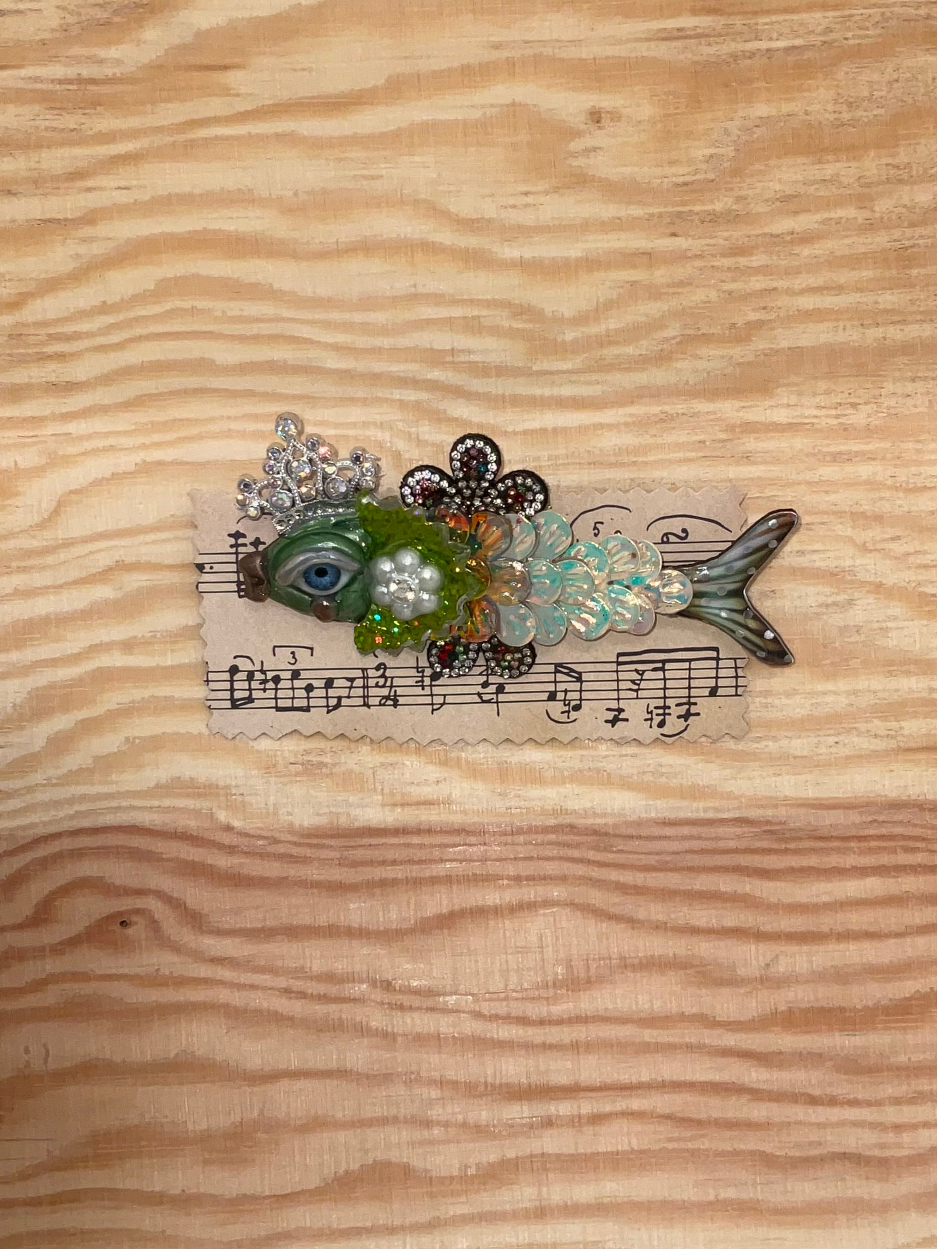Decorative fish-shaped object with floral elements and musical notes on a wooden surface