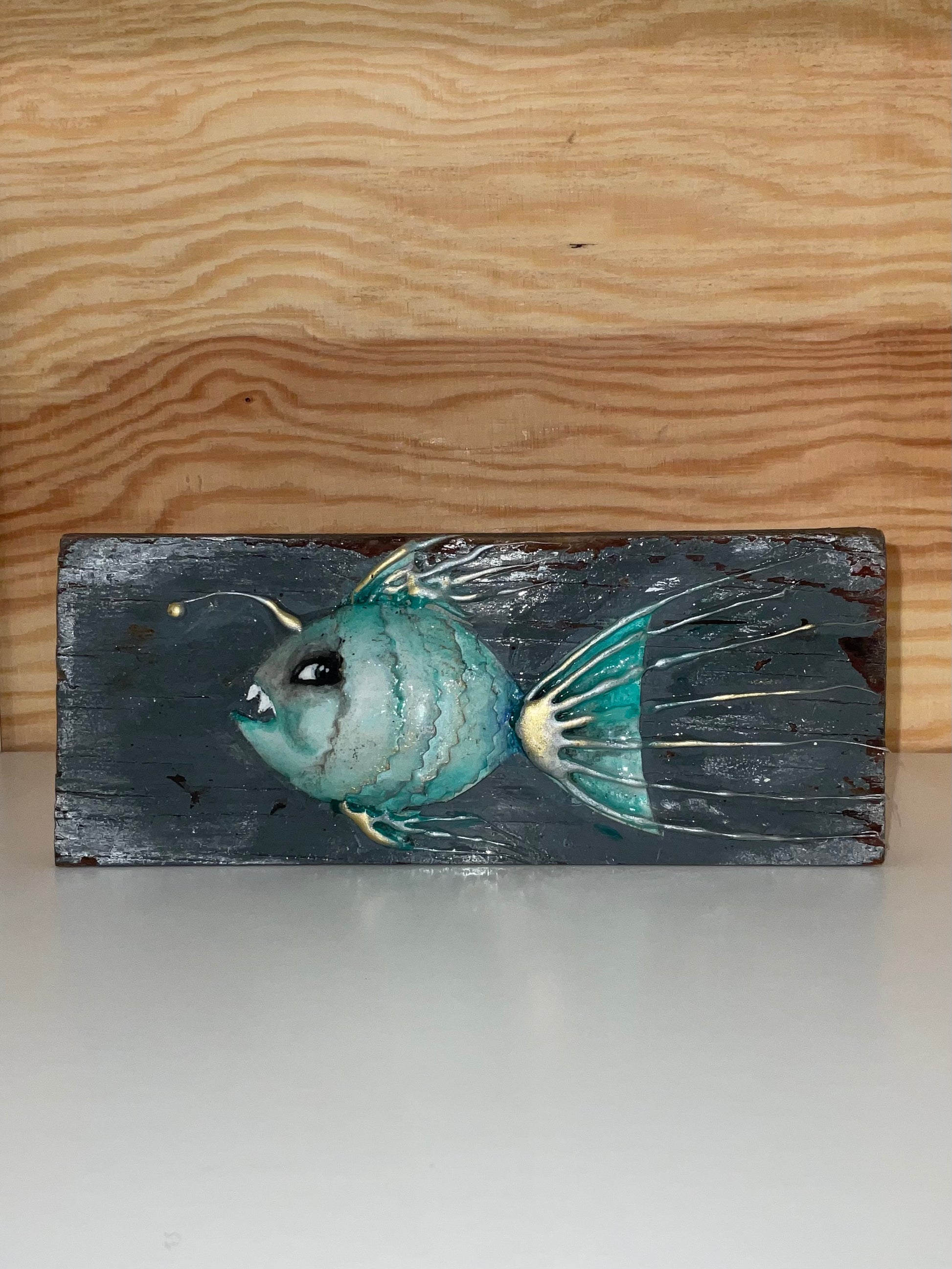 Teal fish sculpture on a wooden block against a wooden background