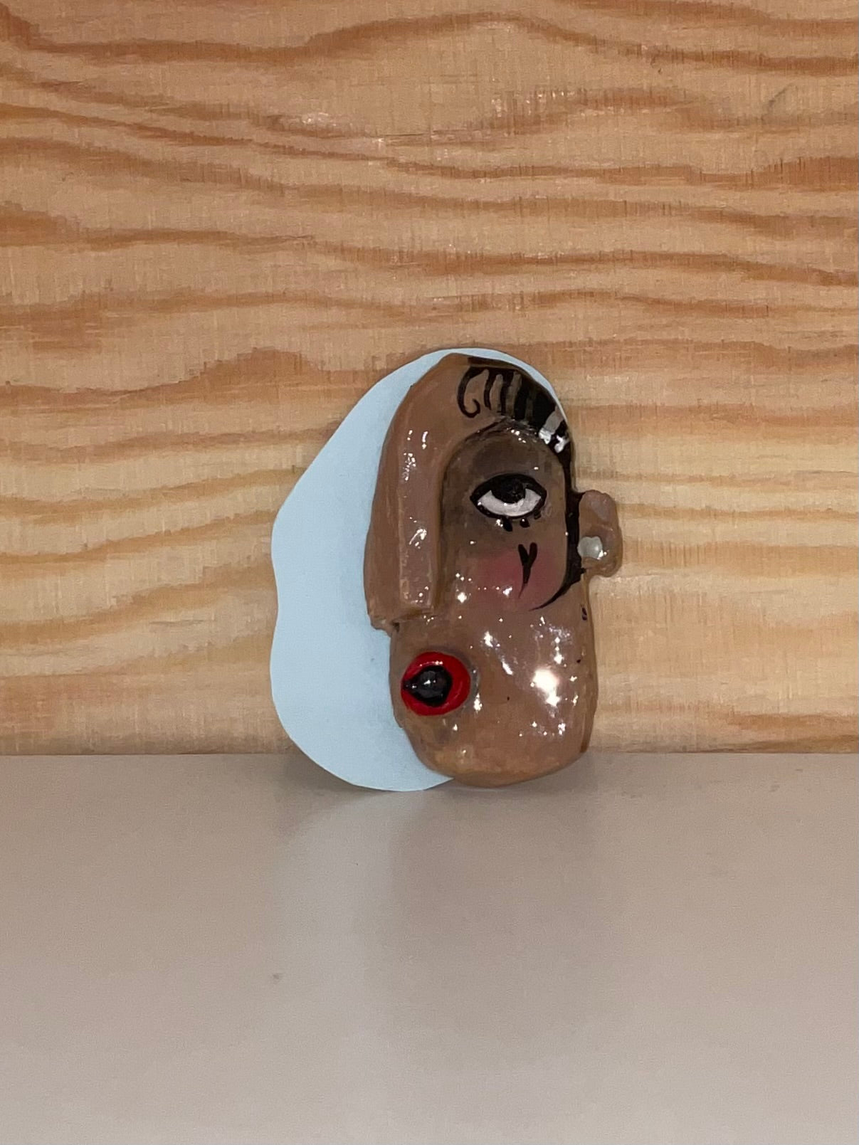 Small brooch of a face with a white base on a wooden surface