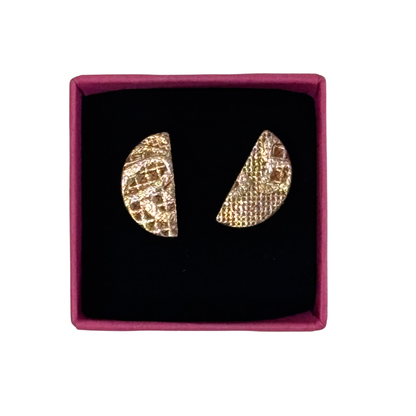 A pair of textured gold crescent-shaped earrings displayed inside a square magenta jewelry box with a black velvet lining, set against a plain white background.