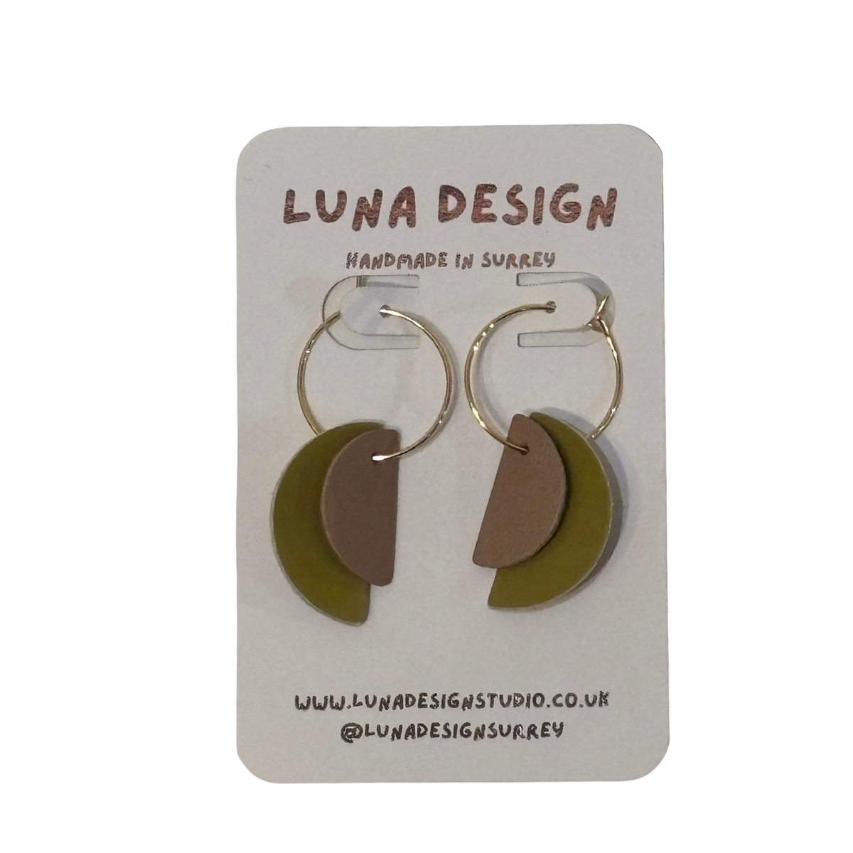 A pair of handmade crescent moon earrings by Luna Design, featuring olive green and taupe half-moons with gold-tone hoops, displayed on a white card backing.