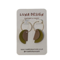 A pair of handmade crescent moon earrings by Luna Design, featuring olive green and taupe half-moons with gold-tone hoops, displayed on a white card backing.