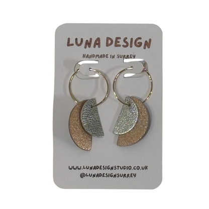 A pair of handmade crescent-shaped hoop earrings by Luna Design, featuring textured metallic gold and silver halves connected by silver wire hoops, displayed on a grey cardboard backing card.