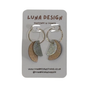 A pair of handmade crescent-shaped hoop earrings by Luna Design, featuring textured metallic gold and silver halves connected by silver wire hoops, displayed on a grey cardboard backing card.