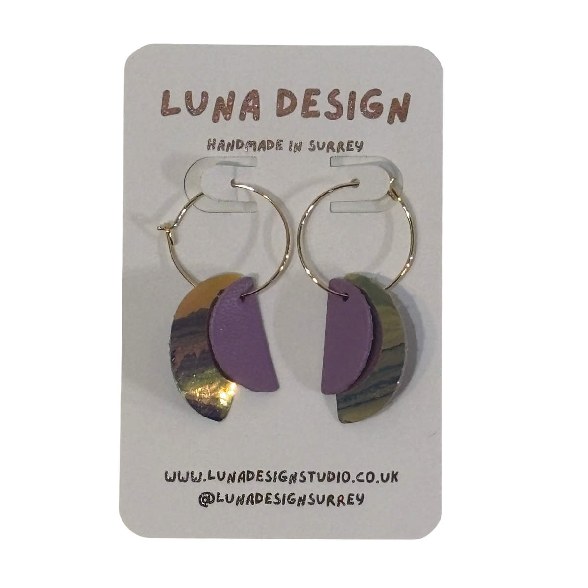 A pair of handmade hoop earrings by Luna Design, featuring purple and iridescent gold crescent moon shapes on gold hoops, displayed on a white backing card.
